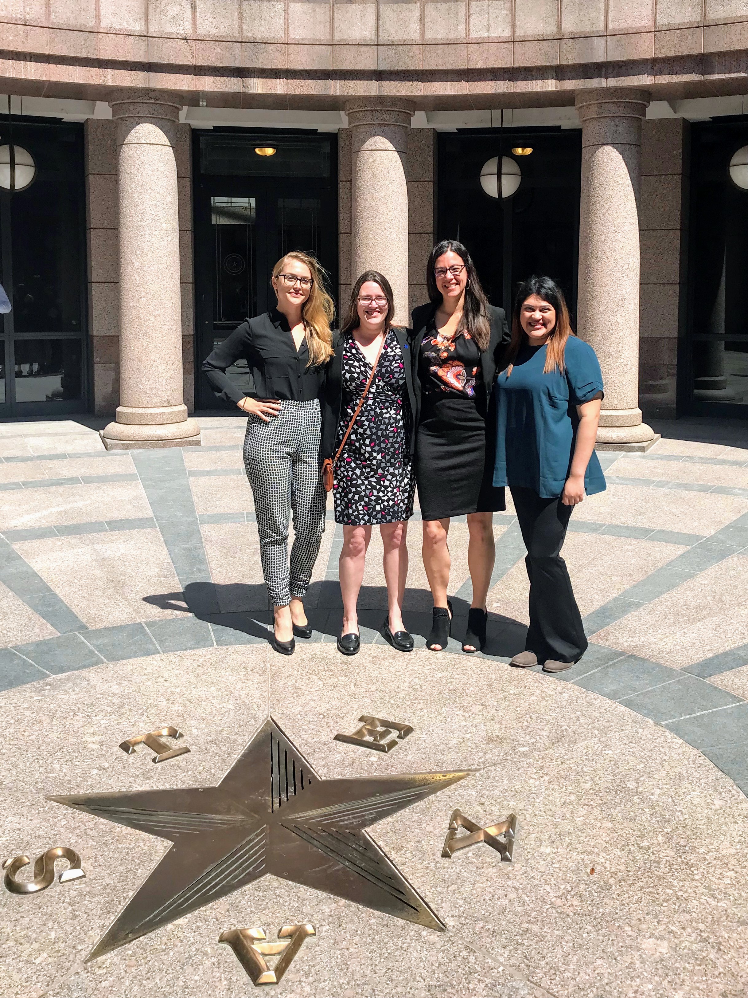 Cuatro personas identificadas como mujeres se encuentran en el interior del Capitolio de Texas. Las letras T, E, X, A y S (presumiblemente en ese orden) rodean una estrella en el suelo.