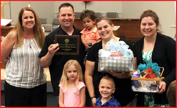 Four adults and three children pose for a photo. One adult is holding a plaque declaring Sara and Doug Mason this year's foster parents of the year.