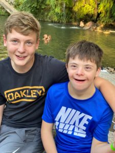 Two young children sitting outside. A small body of water is behind them.