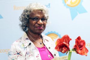 A photo of Frankie Fowler, a longtime SAFE volunteer. She is looking at the camera. A red flower is in the foreground.