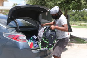 A person carrying backpacks out of the trunk of a car.
