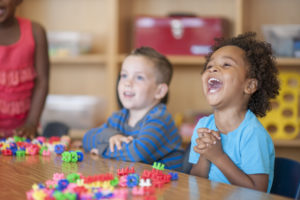 Un grupo multiétnico de niños en edad de primaria juegan juntos con bloques de juguete en una mesa.