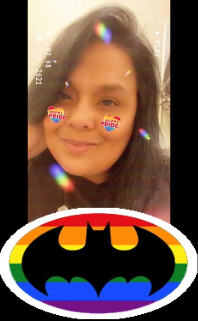 A selfie of a SAFE staffer using a Happy Pride filter. She has dark hair and smiling at the camera. A rainbow heart appears over each of her cheeks with words "Happy PRIDE" on each of them. A large Batman bat symbol is at the bottom of the image with a rainbow behind it.