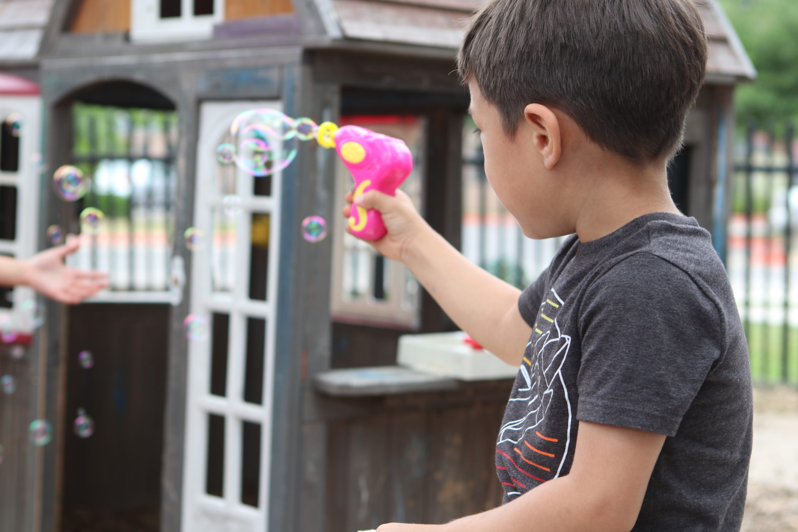 Descripción de la imagen: Foto de un niño sosteniendo una pistola de burbujas rosa. La pistola produce pequeñas burbujas. El niño está de espaldas a la cámara.