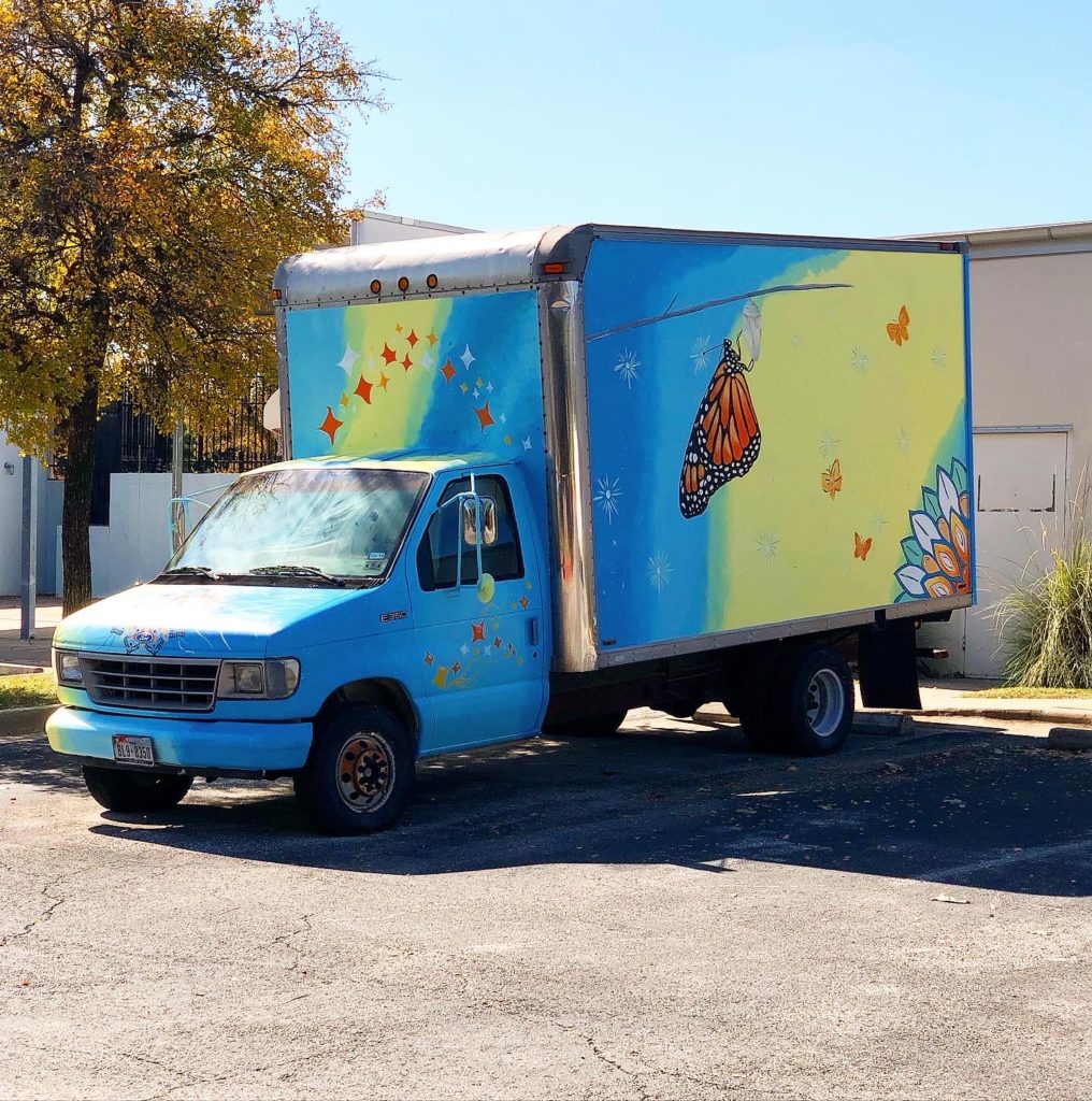 Descripción de la imagen: Un camión pintado de colores. Es principalmente azul y amarillo. Una hermosa mariposa está pintada en el lateral.