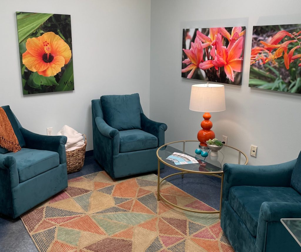 Descripción de la imagen: Una foto de una sala de entrevistas suave, que incluye sillas cómodas, una bonita alfombra, iluminación tenue, agradables cuadros de flores en las paredes y un difusor de aceite.