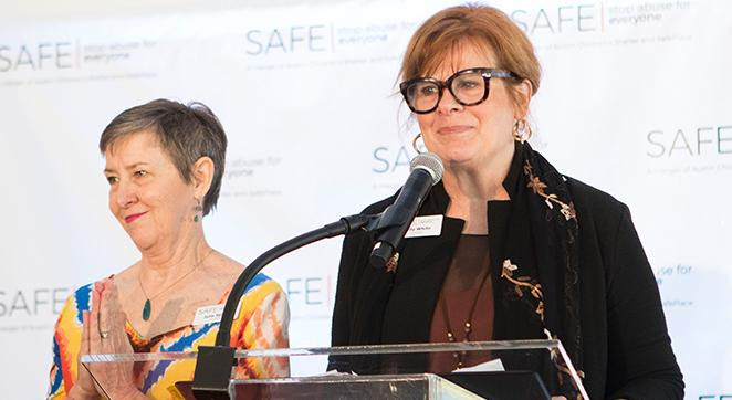 Image description: A photo of SAFE Co-CEOs Kelly White and Julia Spann. Kelly is standing at a podium with a microphone in front of her. Julia is at her side.