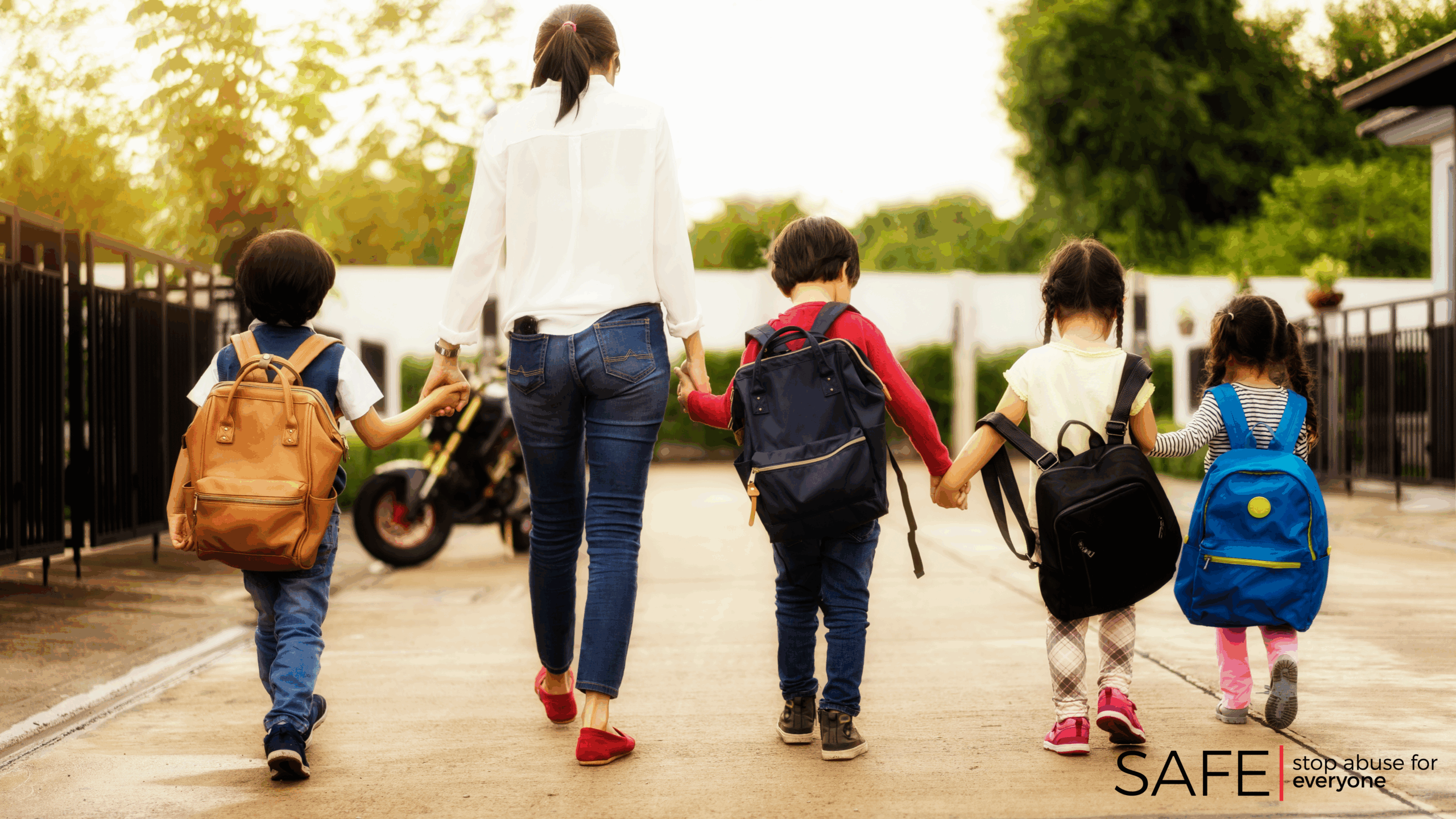 Image description: A stock photograph of a woman and four children walking. They are all holding hands. Their backs are facing the camera.